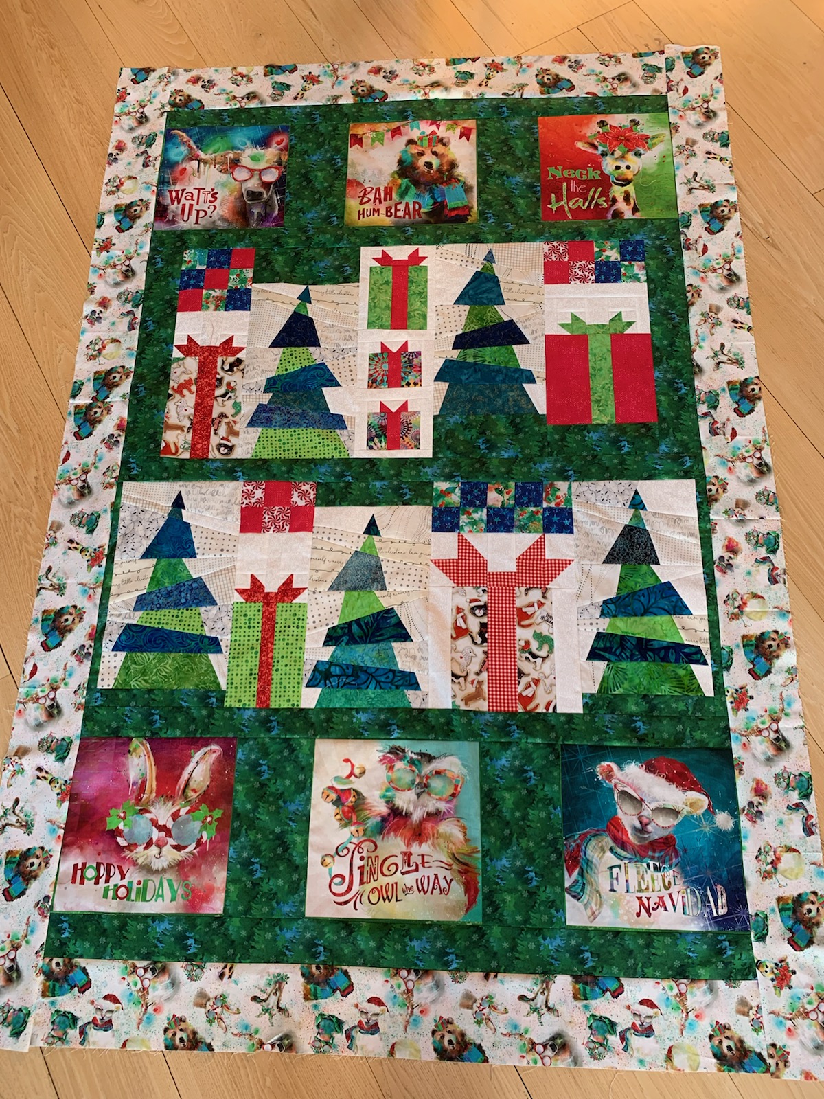 Quilt with dark green christmas trees, red presents with bows, and cute animals wearing santa hats