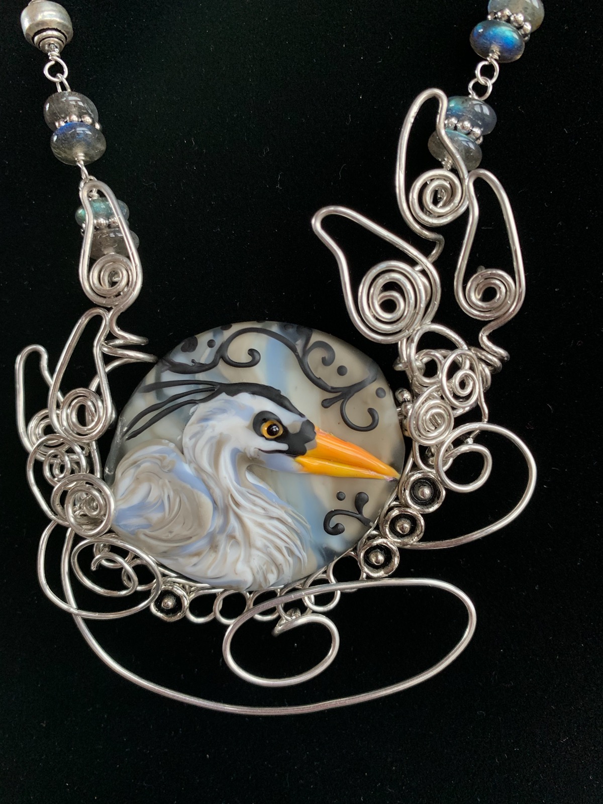 Glass bead by Keri Fuhr featring a grey heron head with yellow beak set in scrolls and spirals of silver wire by Melanie Schow
